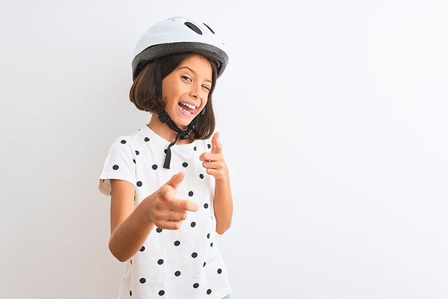 Beautiful child girl wearing security bike helmet standing over isolated white background pointing fingers to camera with happy and funny face. Good energy and vibes.