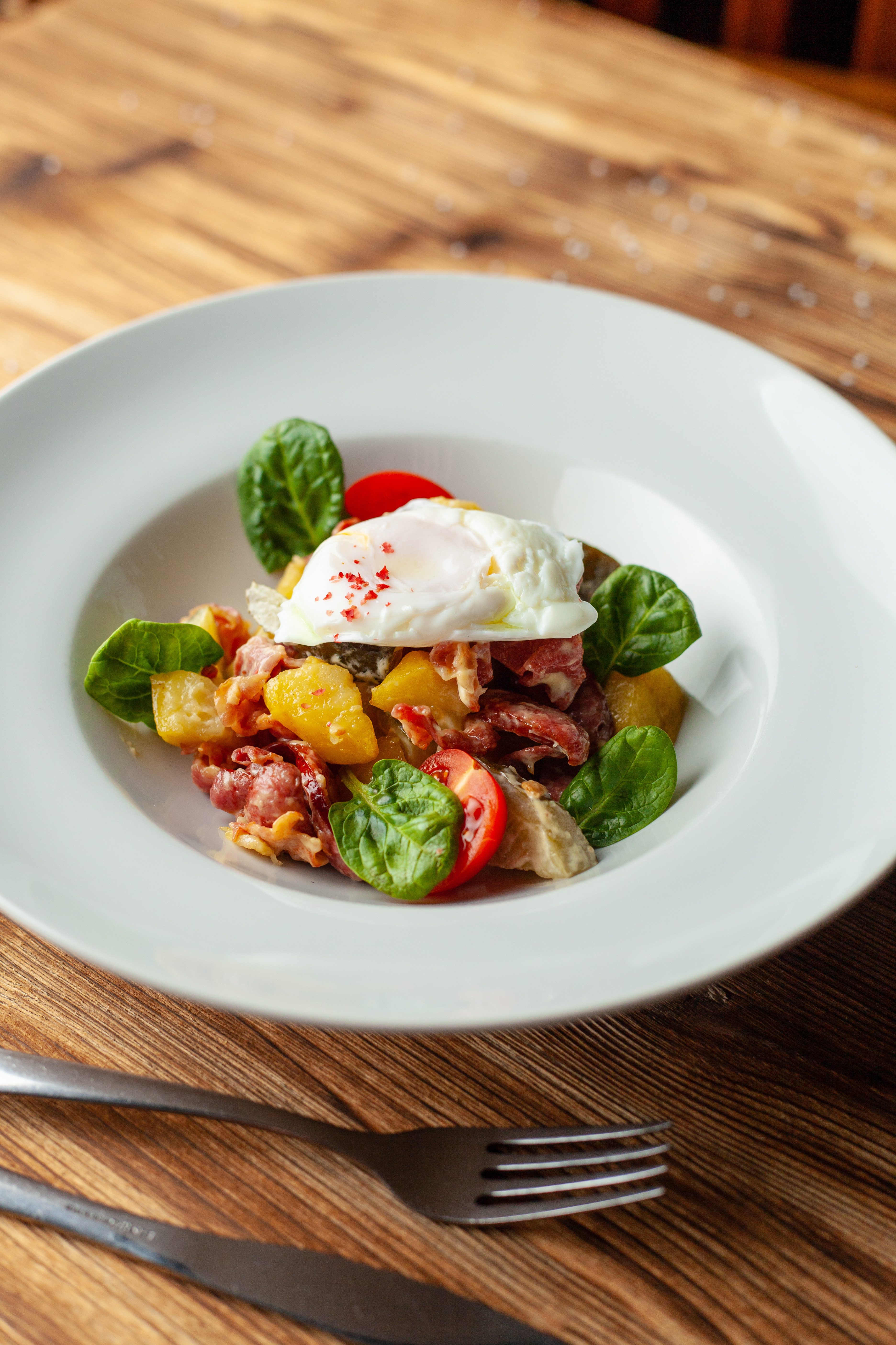 Rustic salad with, tomatoes, chorizo sausage, poached egg, spinach, potato and pickled cucumber for nutritious dinner, served on wooden table