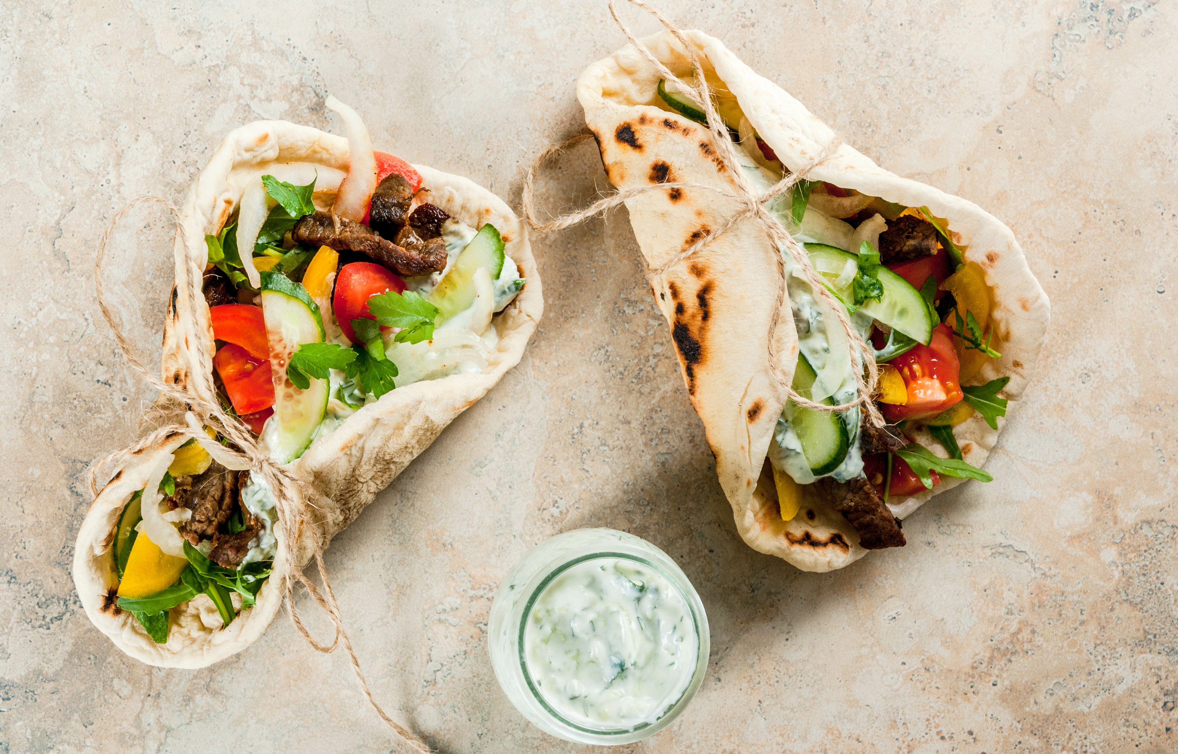 Healthy snack, lunch. Traditional Greek wrapped sandwich gyros - tortillas, bread pita with a filling of vegetables, beef meat and sauce tzatziki. On light stone table Copy space top view, Healthy snack, lunch. Traditional Greek wrapped sandwich gyros -