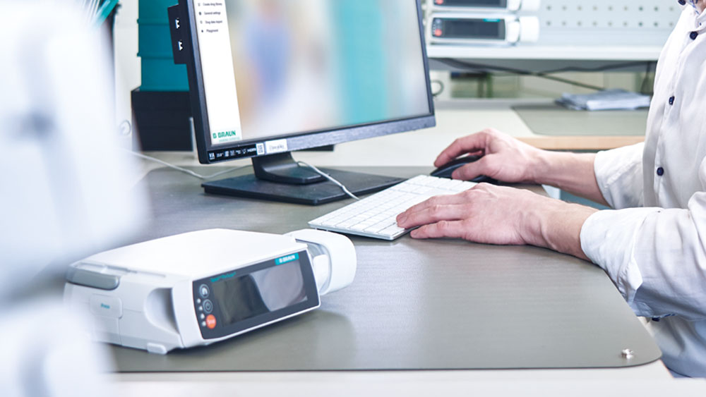 Henkilö istuu tietokoneen edessä – työpöydällä on myös infuusiopumppu